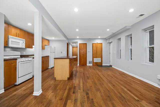 a view of an empty room and kitchen with wooden floor