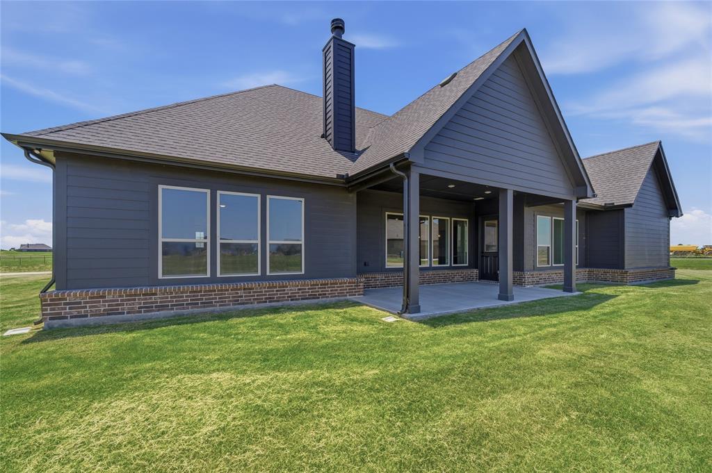 2305 Gypsum Street Krum, TX 76249 - Photo 23 of 26 Expansive green lawn surrounds a modern residence featuring dark siding and a prominent covered patio with supporting columns