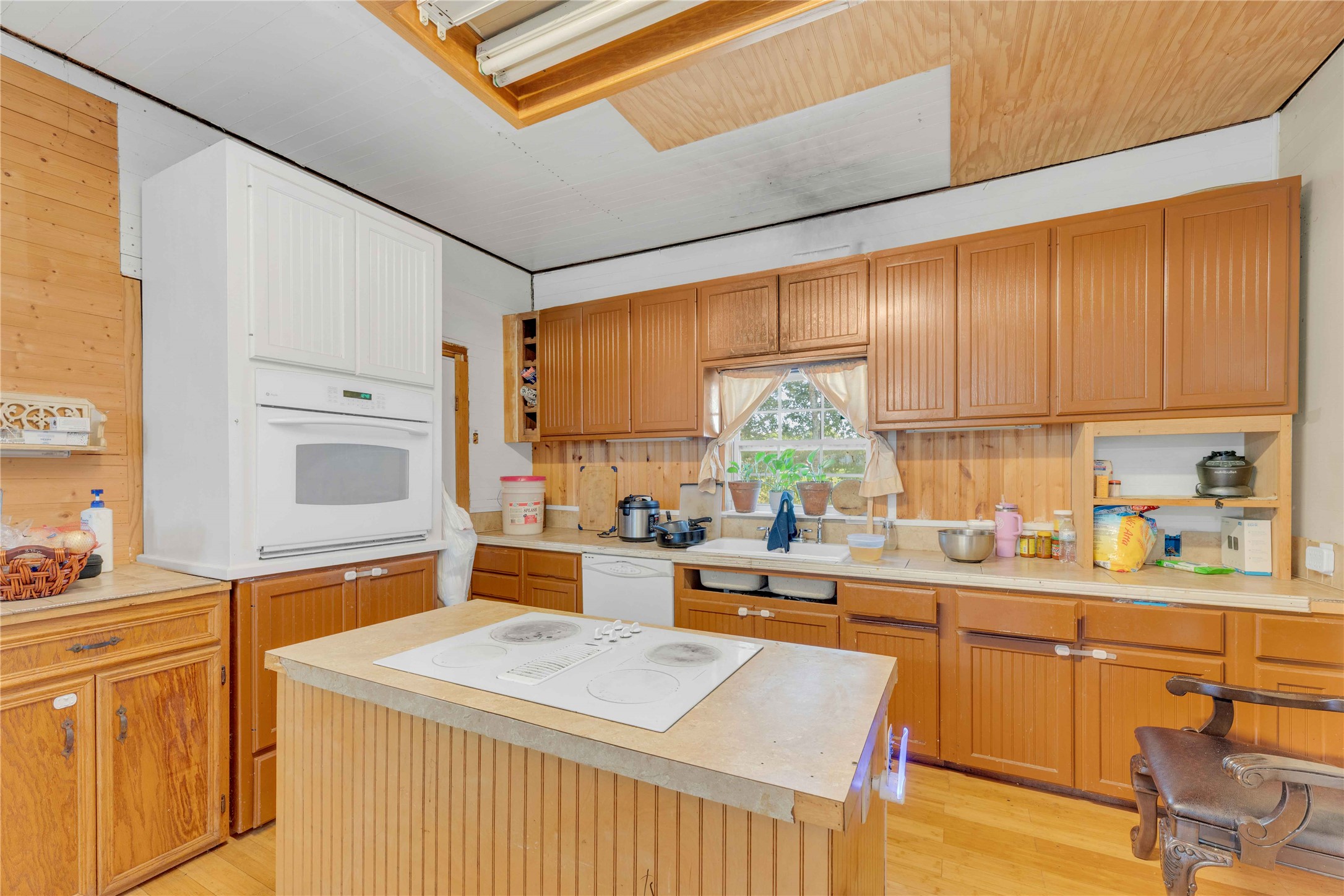 20235 Engelmann Lane Manor, TX 78653 - Photo 23 of 34 Kitchen with light countertops, light wood-type flooring, white appliances, a center island, and wooden walls