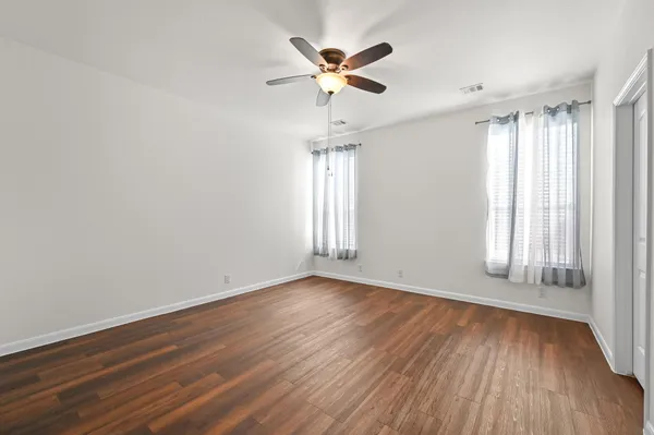 an empty room with wooden floor chandelier fan and windows