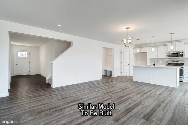 an empty room with wooden floor and kitchen view