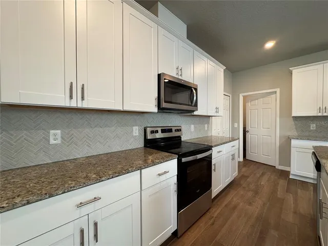 a kitchen with granite countertop a sink a stove top oven and cabinetry