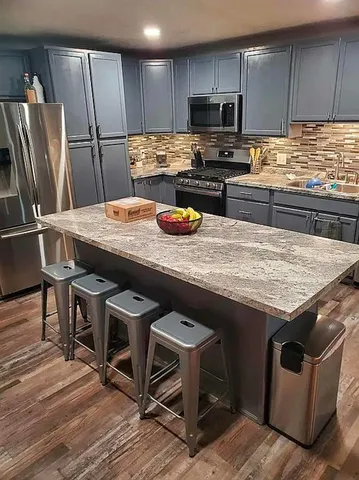 a kitchen with stainless steel appliances kitchen island granite countertop a table chairs stove and refrigerator