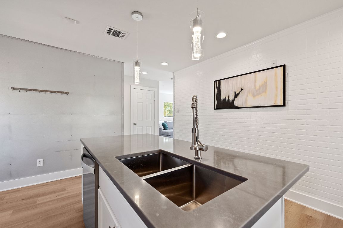 1171 Nickols Avenue, Unit 1 Austin, TX 78721 - Photo 12 of 22 Kitchen featuring decorative light fixtures, brick wall, white cabinets, light wood-style flooring, and stainless steel dishwasher