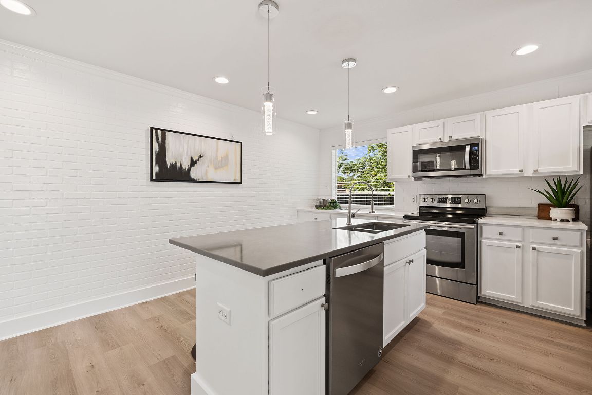 1171 Nickols Avenue, Unit 1 Austin, TX 78721 - Photo 10 of 22 Kitchen with stainless steel appliances, white cabinets, a center island with sink, light wood-style floors, and hanging light fixtures