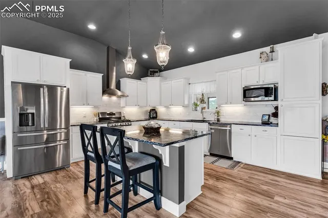 a kitchen with kitchen island granite countertop wooden floors white cabinets and stainless steel appliances