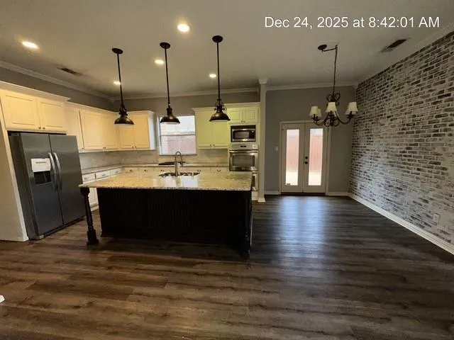 a kitchen with stainless steel appliances kitchen island granite countertop a refrigerator a stove and oven with wooden floor