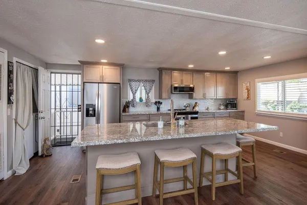 a kitchen with stainless steel appliances granite countertop a refrigerator a sink dishwasher a stove and white cabinets with wooden floor