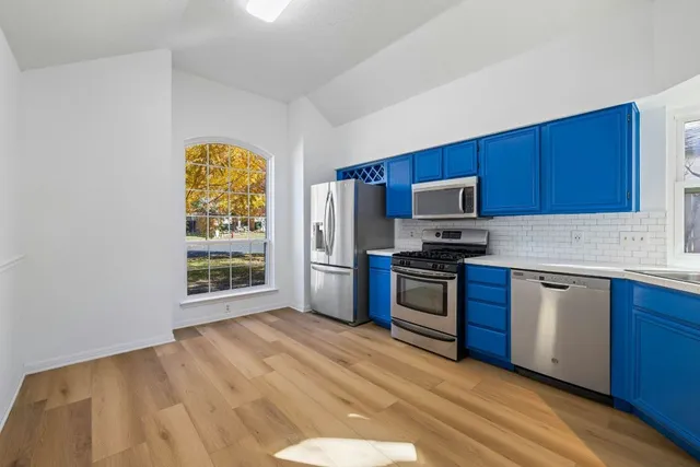 a kitchen with granite countertop wooden floors stainless steel appliances and a window