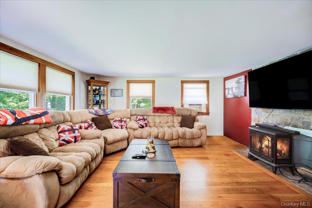 10-12 Woodlea Road Salt Point, NY 12578 - Photo 8 of 48 Living area featuring wood-finish flooring, multiple windows with natural wood trim, a stone-faced hearth, and a freestanding fireplace