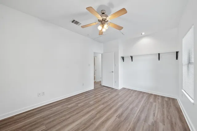 an empty room with wooden floor fan and windows