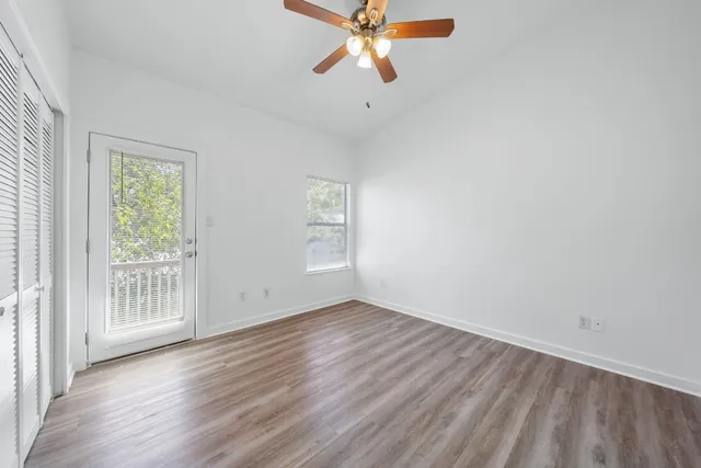 an empty room with wooden floor fan and windows