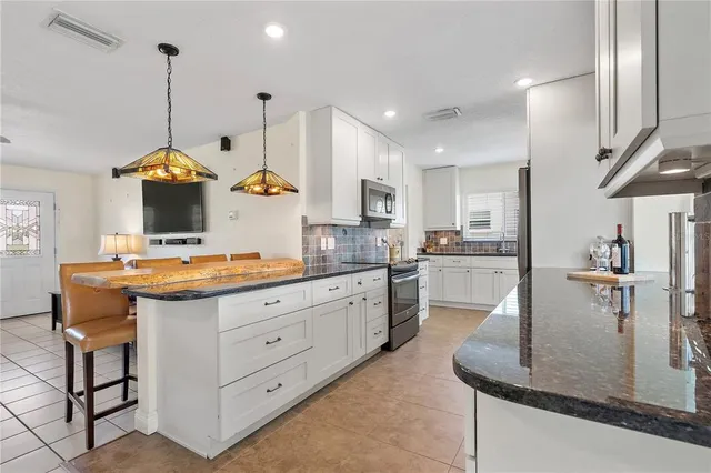 a kitchen with kitchen island granite countertop a stove a sink a oven and a living room view
