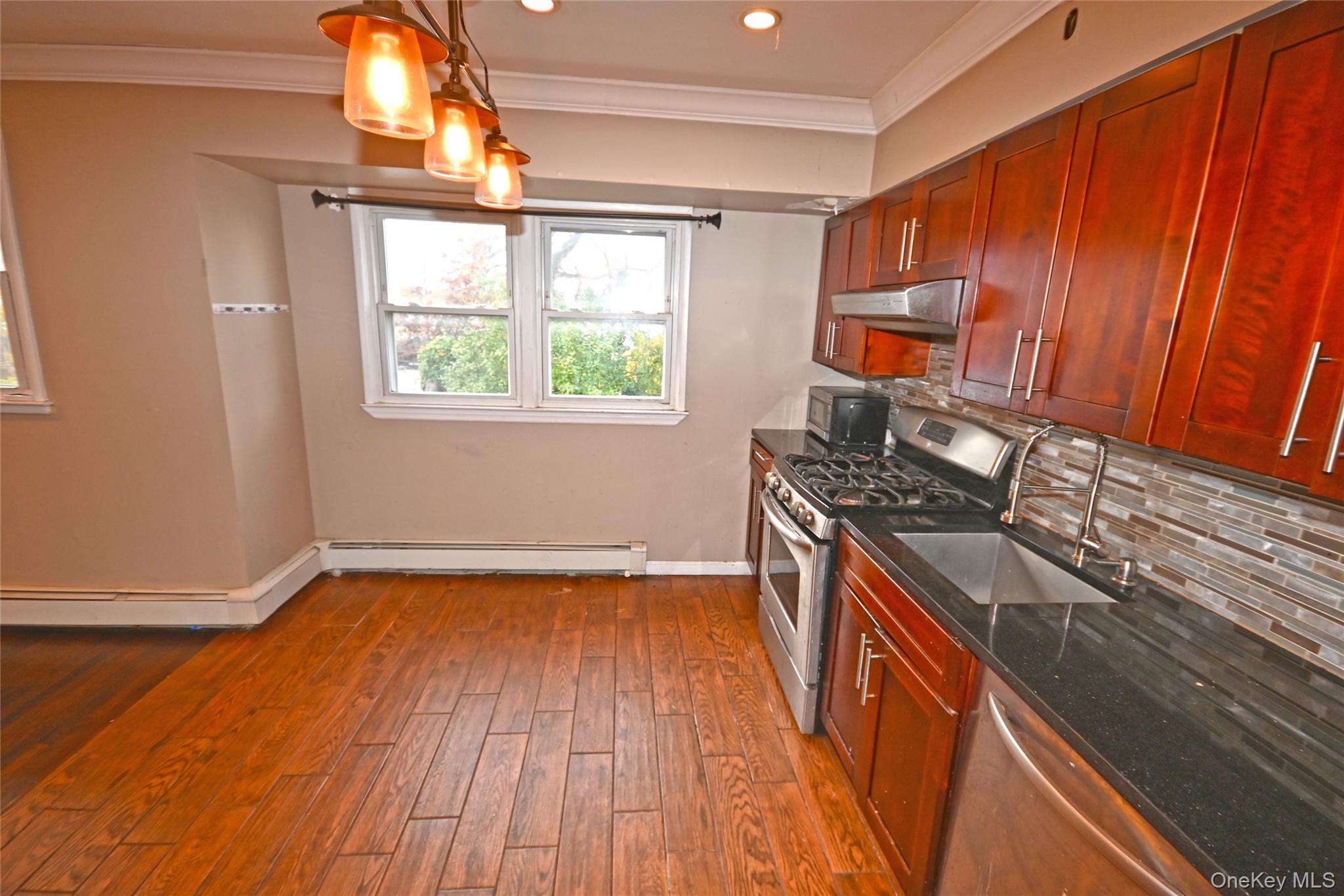 89 Osborne Road West Hempstead, NY 11552 - Photo 36 of 50 Kitchen featuring stainless steel appliances, dark stone countertops, crown molding, decorative backsplash, and hanging light fixtures