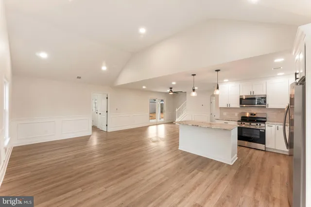 a large kitchen with stainless steel appliances a large counter top a stove a sink dishwasher and a refrigerator with wooden floor