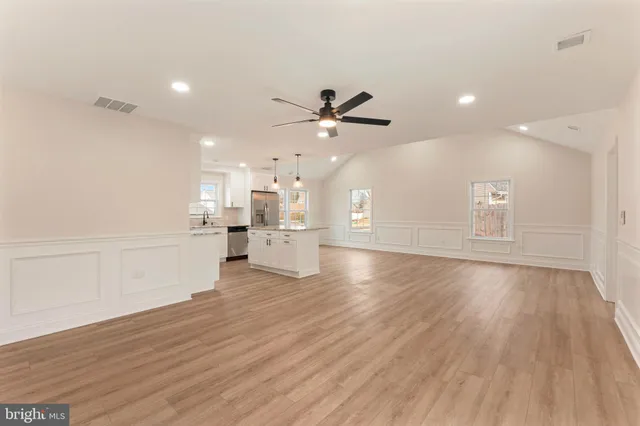 a view of an empty room and kitchen with wooden floor