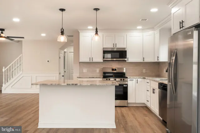 a kitchen with stainless steel appliances granite countertop a sink a stove a refrigerator and island with wooden floor