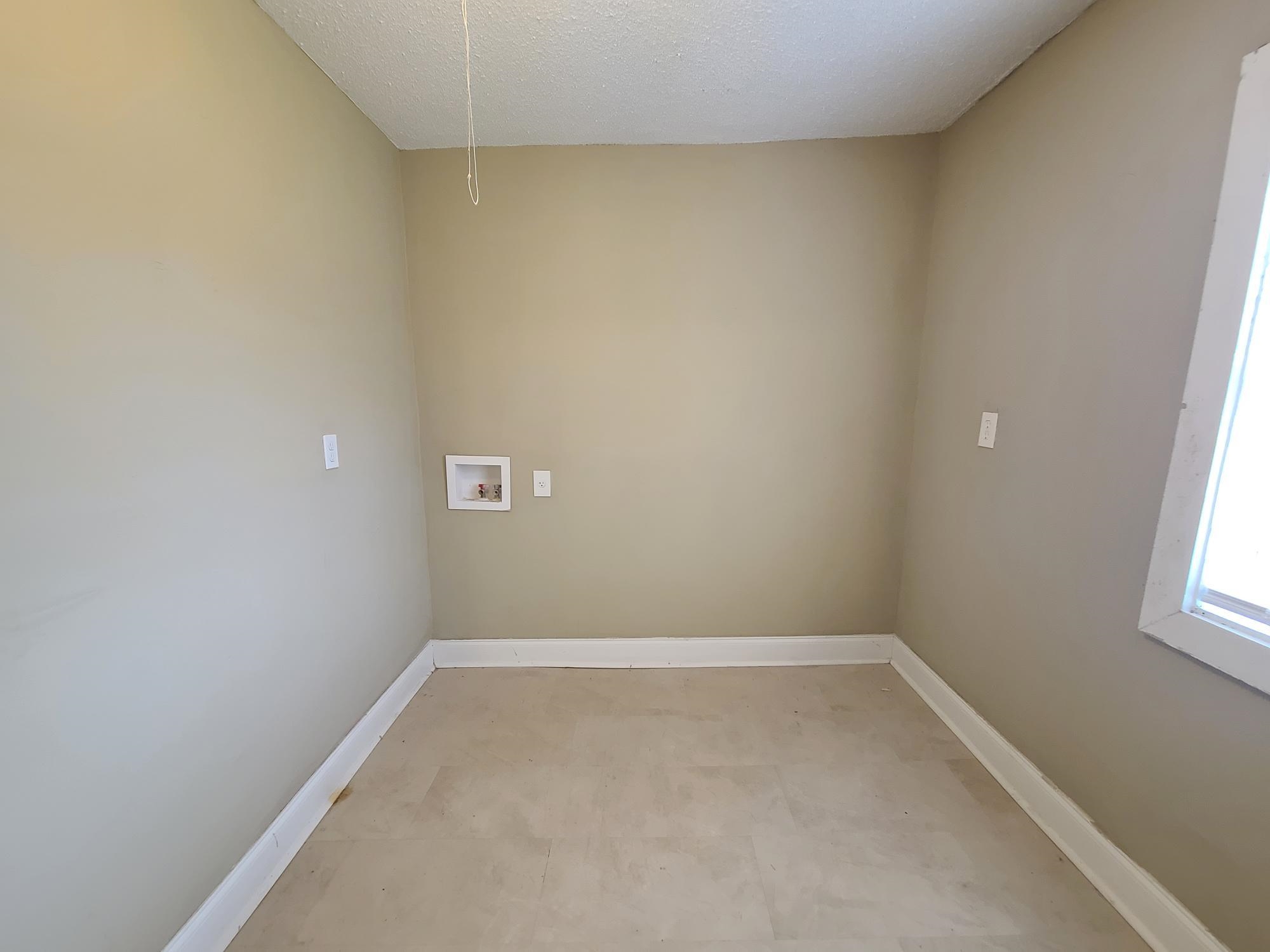Neutral tone wall paint, light-colored flooring, window with white trim, and a utility hookup