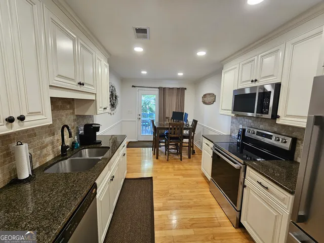a kitchen with stainless steel appliances granite countertop wooden cabinets a sink dishwasher a stove and a microwave oven with wooden floor