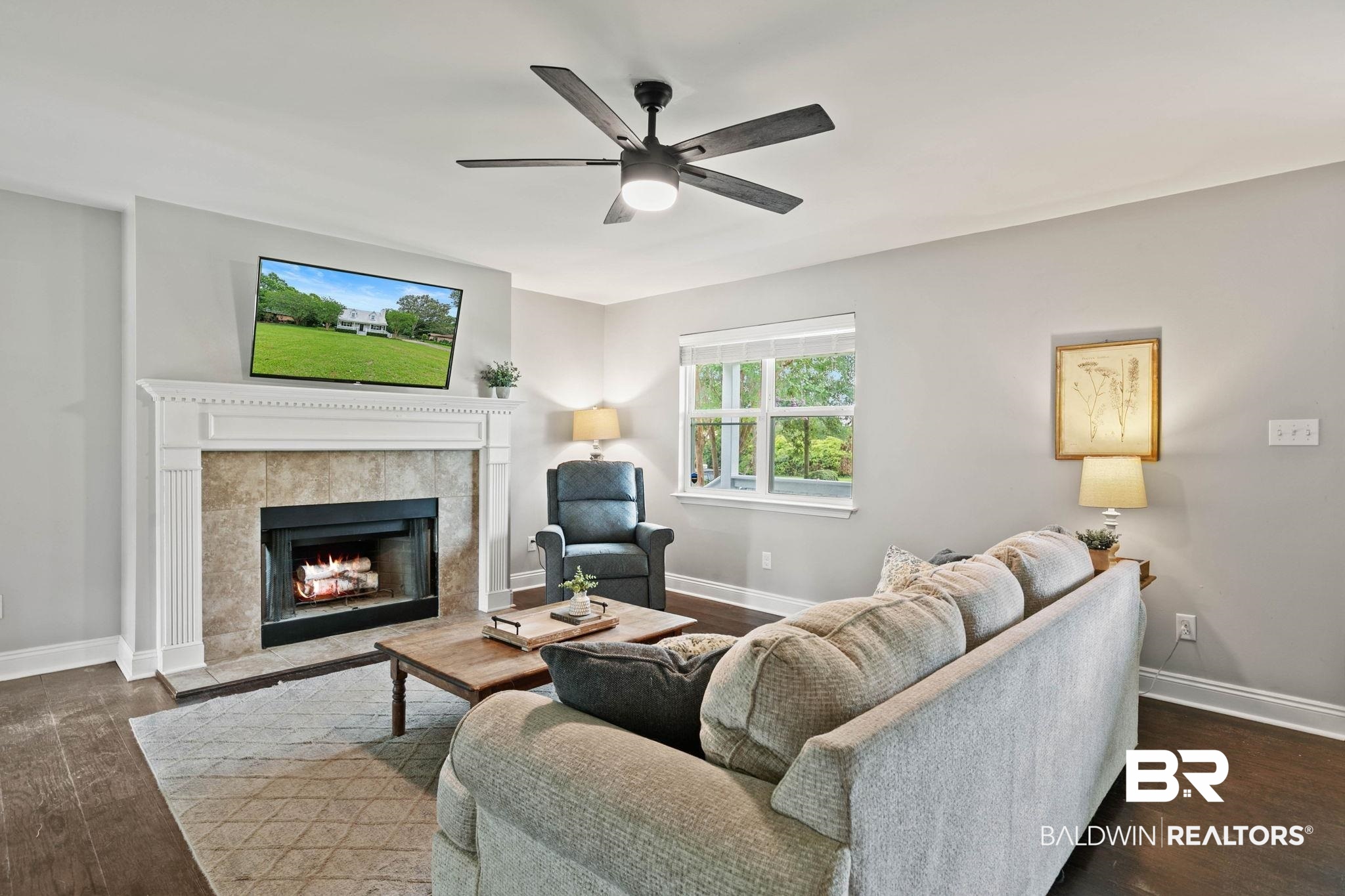22810 High Ridge Road Fairhope, AL 36532 - Photo 20 of 78 Living area featuring a tile-surround fireplace with a classic mantel, wood-finish flooring, a ceiling fan with integrated lighting, and multiple windows
