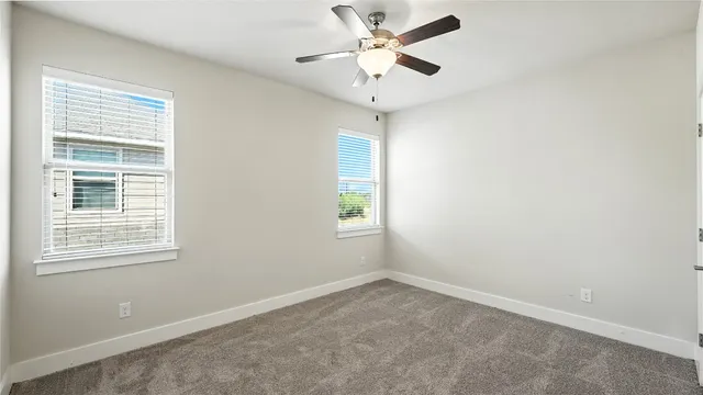 an empty room with a chandelier fan and windows