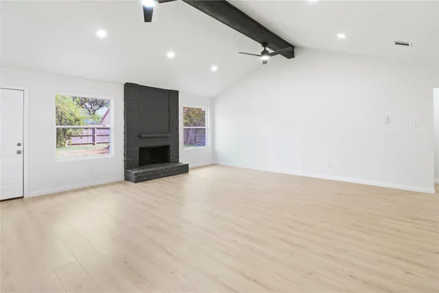 an empty room with wooden floor fireplace and windows