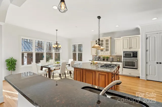 a kitchen with stainless steel appliances granite countertop a stove top oven a sink dishwasher and white cabinets with wooden floor