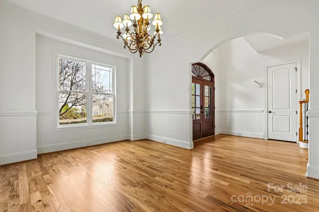an empty room with wooden floor chandelier and windows