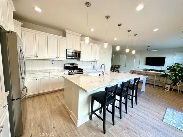 a kitchen with stainless steel appliances kitchen island granite countertop a stove a sink a refrigerator and a dining table with wooden floor