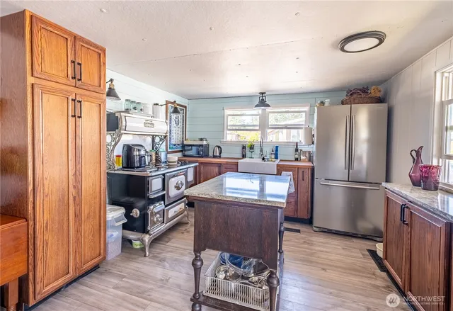 a kitchen with stainless steel appliances granite countertop a refrigerator a sink dishwasher a dining table and chairs with wooden floor