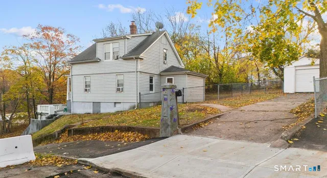 a view of a white house next to a yard with big trees