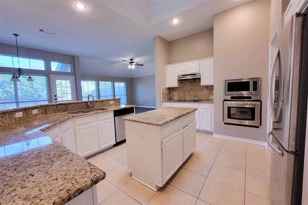 1604 Knoll Ridge Circle Corinth, TX 76210 - Photo 13 of 37 Open-concept kitchen featuring an island, white cabinetry, integrated stainless steel appliances, a tile backsplash, and light-toned tile flooring