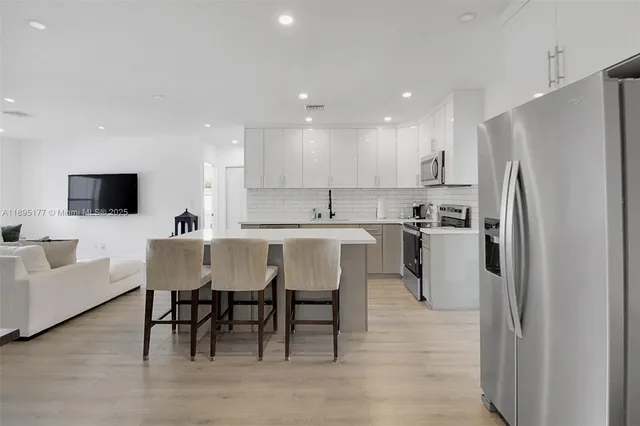 a kitchen with stainless steel appliances granite countertop a dining table chairs refrigerator and sink