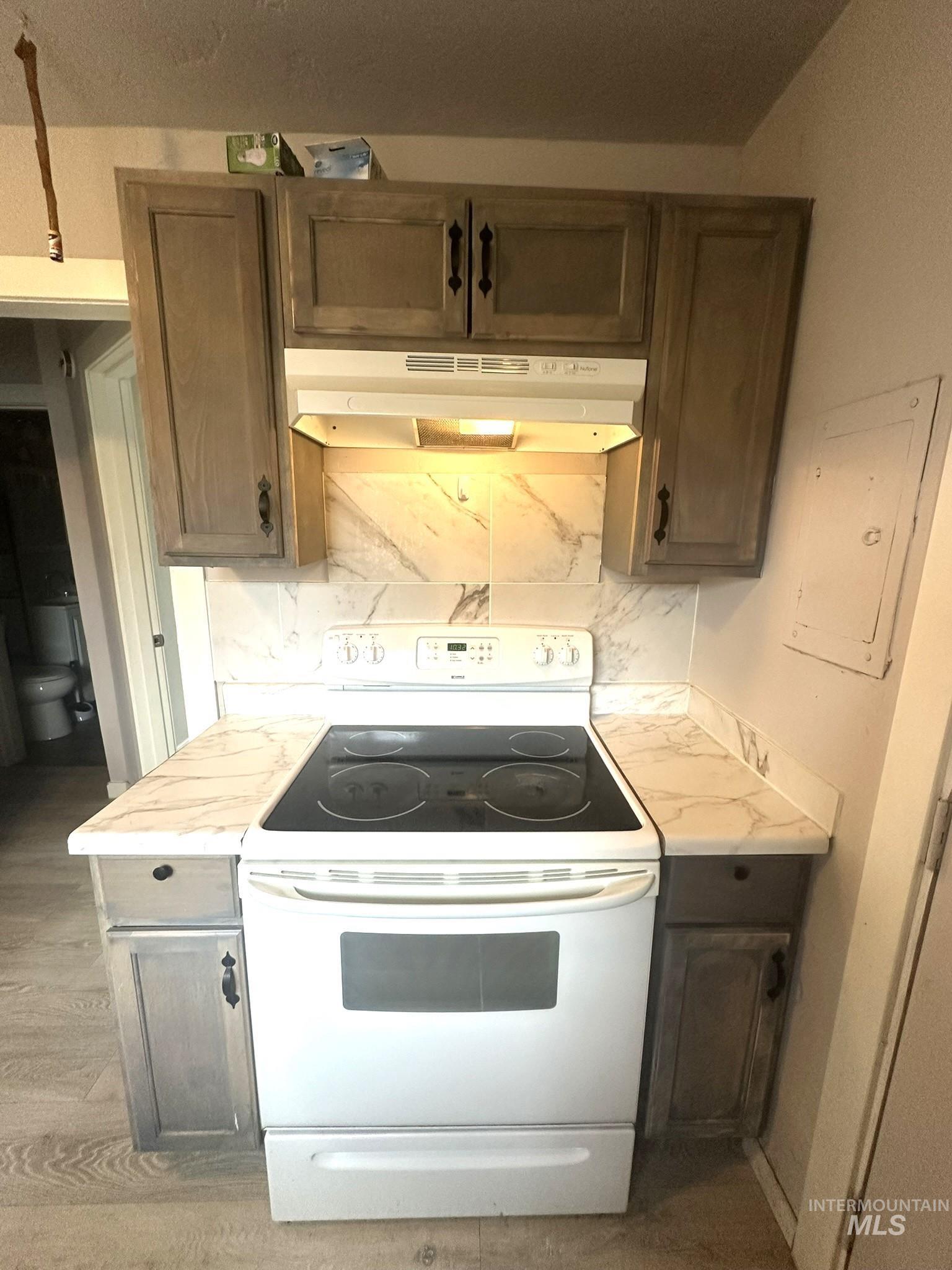 811 East Liberty Street Weiser, ID 83672 - Photo 11 of 12 Kitchen with white range with electric cooktop, light countertops, electric panel, decorative backsplash, and dark wood finish cabinetry