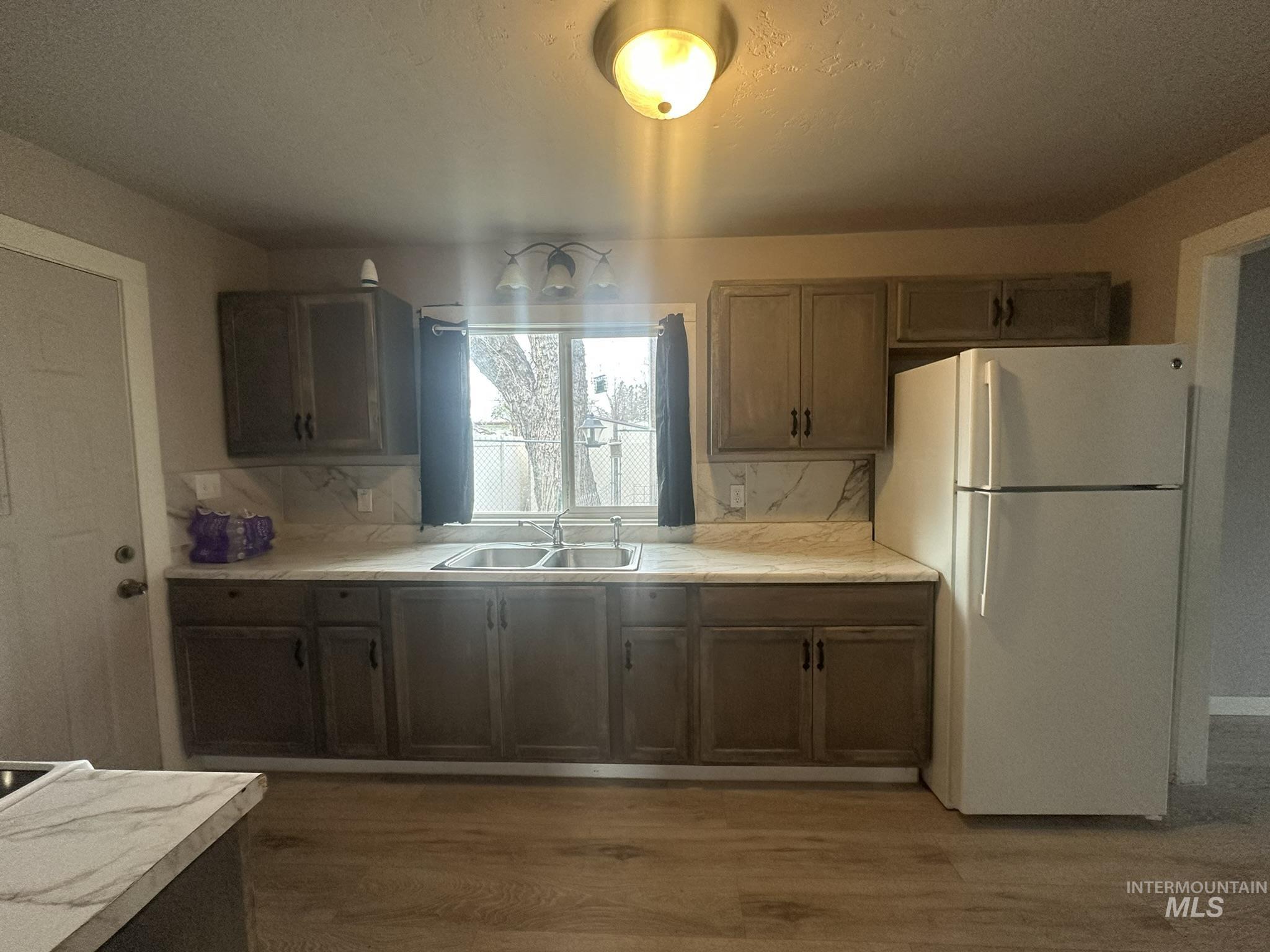 811 East Liberty Street Weiser, ID 83672 - Photo 10 of 12 Kitchen featuring freestanding refrigerator, light countertops, dark wood-type flooring, backsplash, and a textured ceiling