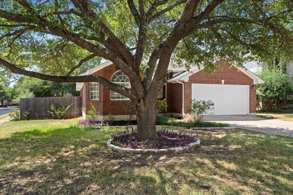 Mature shade trees frame the classic brick exterior and attached garage of this single-family residence.