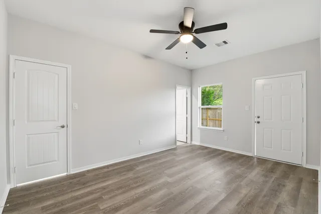 an empty room with wooden floor ceiling fan and windows