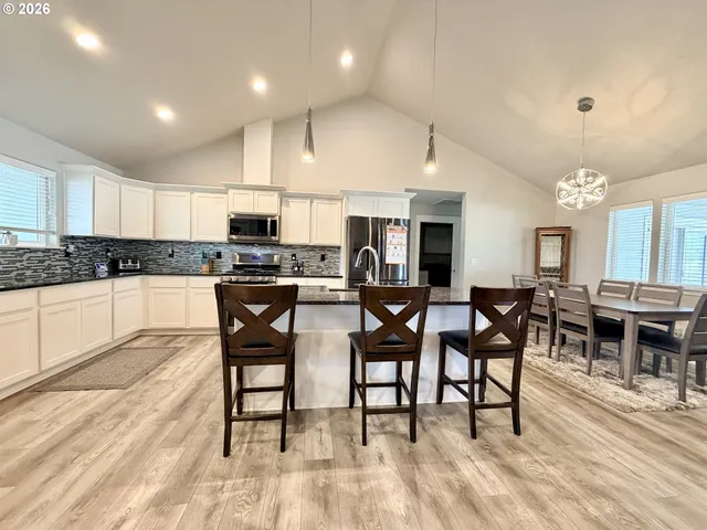 a kitchen with stainless steel appliances granite countertop a stove top oven a sink a dining table and chairs with wooden floor