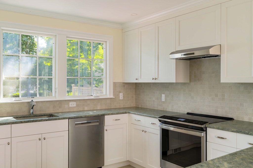 a kitchen with granite countertop a sink stainless steel appliances white cabinets and a window