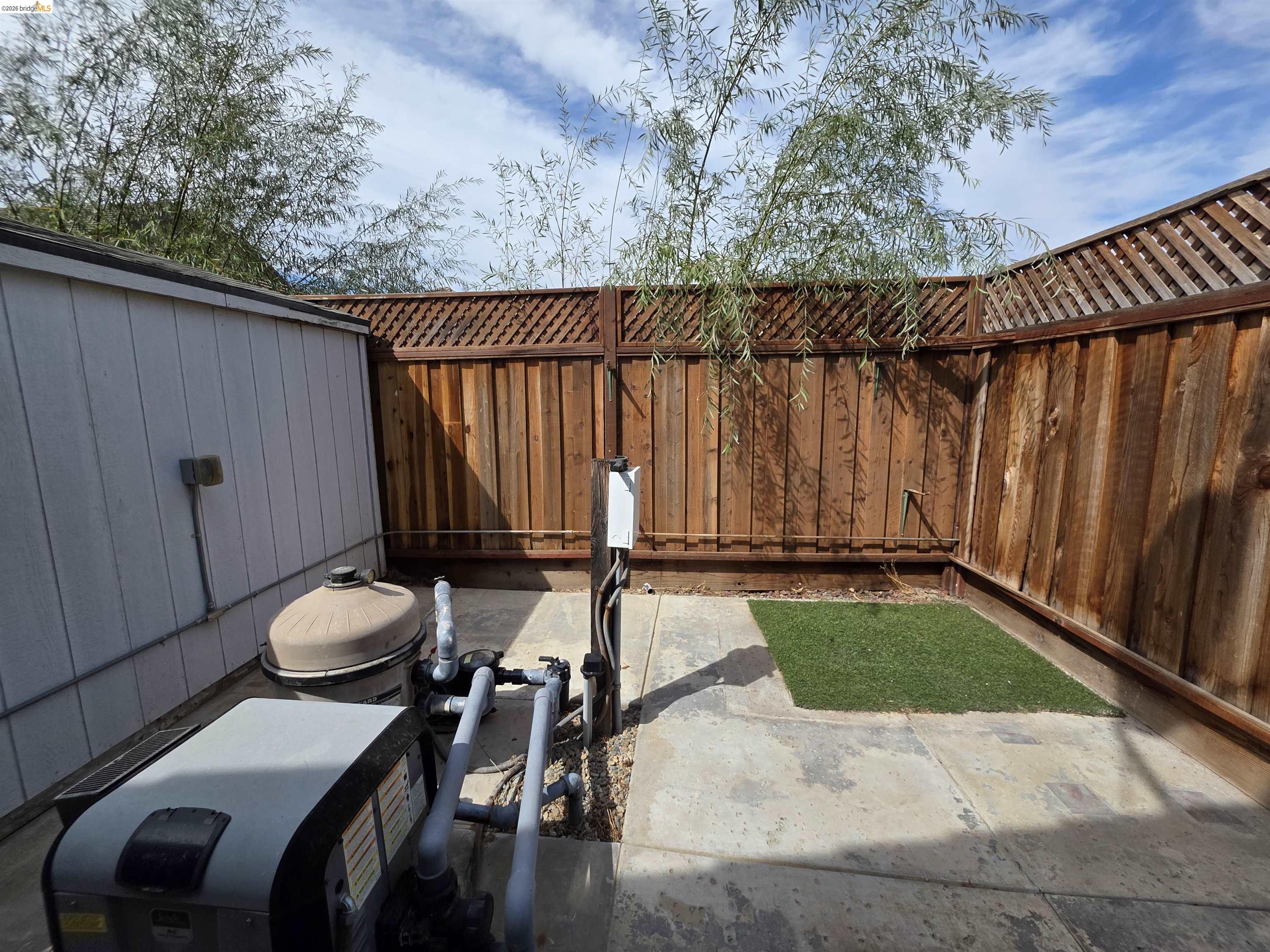 2607 Glow Road Riverbank, CA 95367 - Photo 40 of 42 Paved courtyard featuring a perimeter wood fence with lattice top, artificial turf accent, and property utility equipment