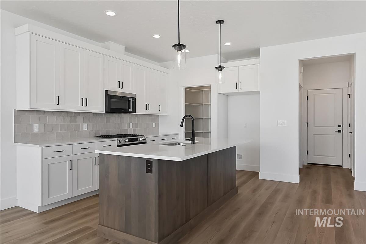 776 South Calhoun Lane Star, ID 83669 - Photo 4 of 49 Contemporary kitchen featuring a large central island with a solid surface countertop, white shaker-style cabinetry, stainless steel appliances, and wood-finish flooring