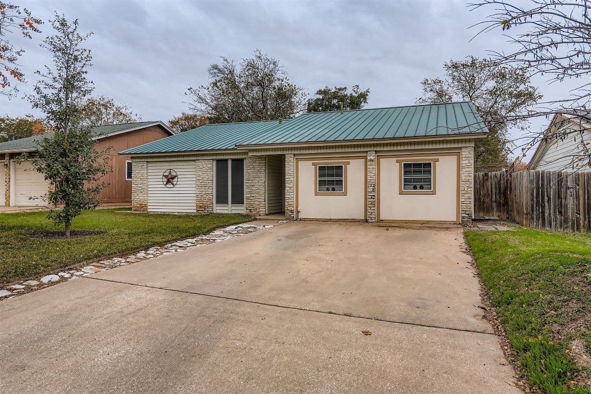 Ranch-style home with a metal roof, stone siding, and driveway