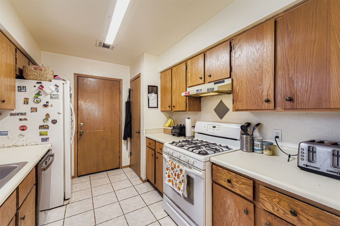 3104 Dominic Drive Austin, TX 78745 - Photo 12 of 28 Kitchen featuring white gas stove, brown cabinetry, light countertops, and light tile patterned flooring