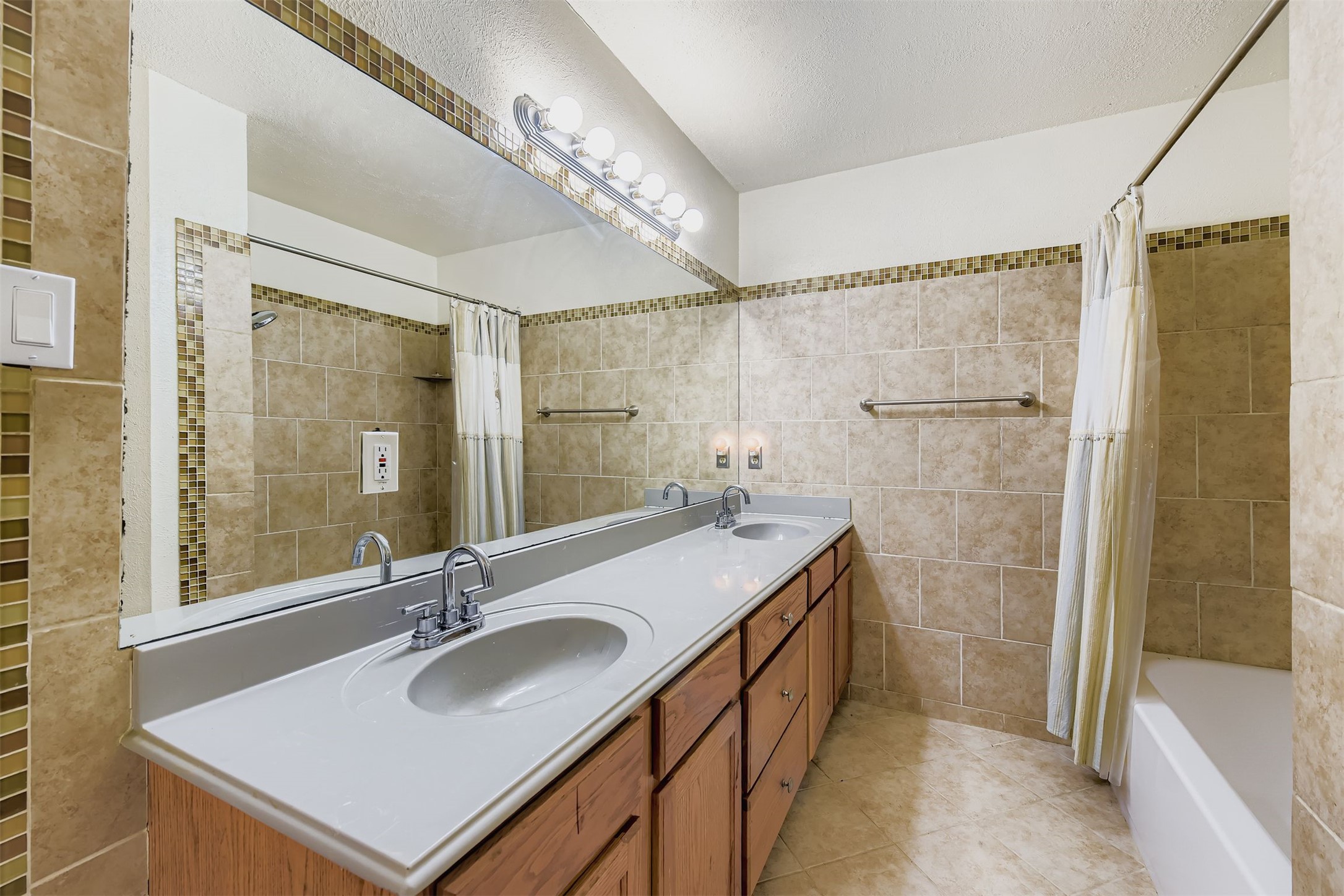 3104 Dominic Drive Austin, TX 78745 - Photo 16 of 28 Bathroom featuring double vanity, shower / bath combo with shower curtain, tile walls, light tile patterned floors, and a textured ceiling