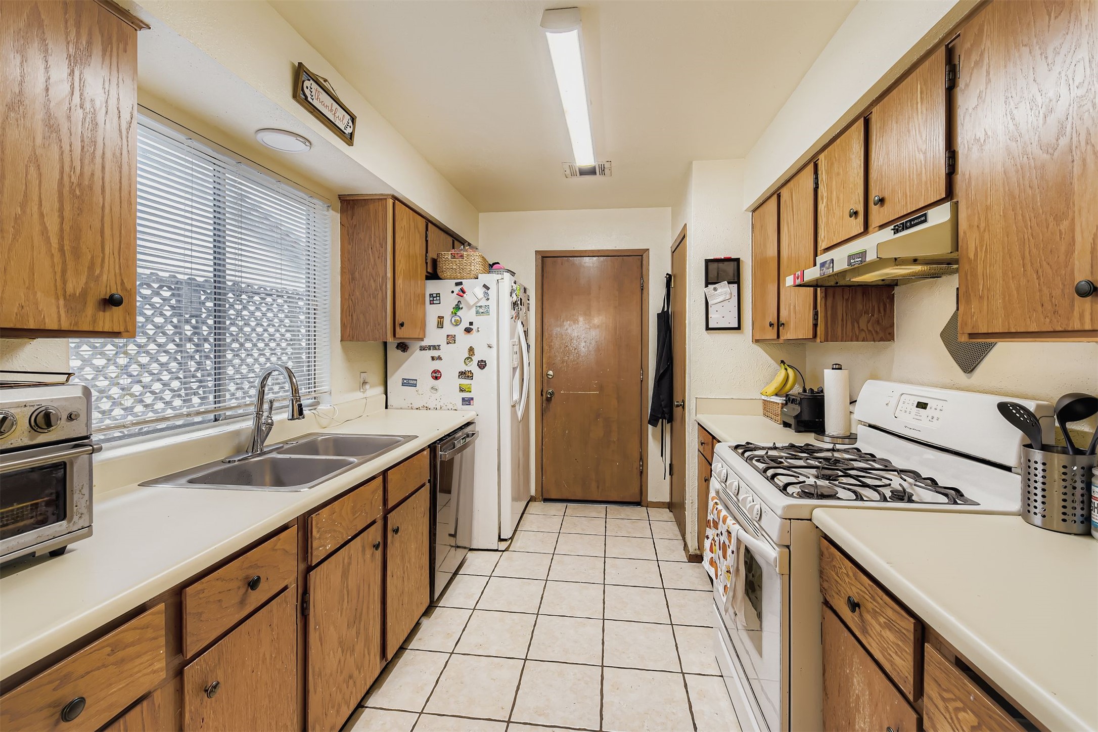 3104 Dominic Drive Austin, TX 78745 - Photo 10 of 28 Kitchen featuring white gas stove, brown cabinets, light countertops, under cabinet range hood, and dishwasher