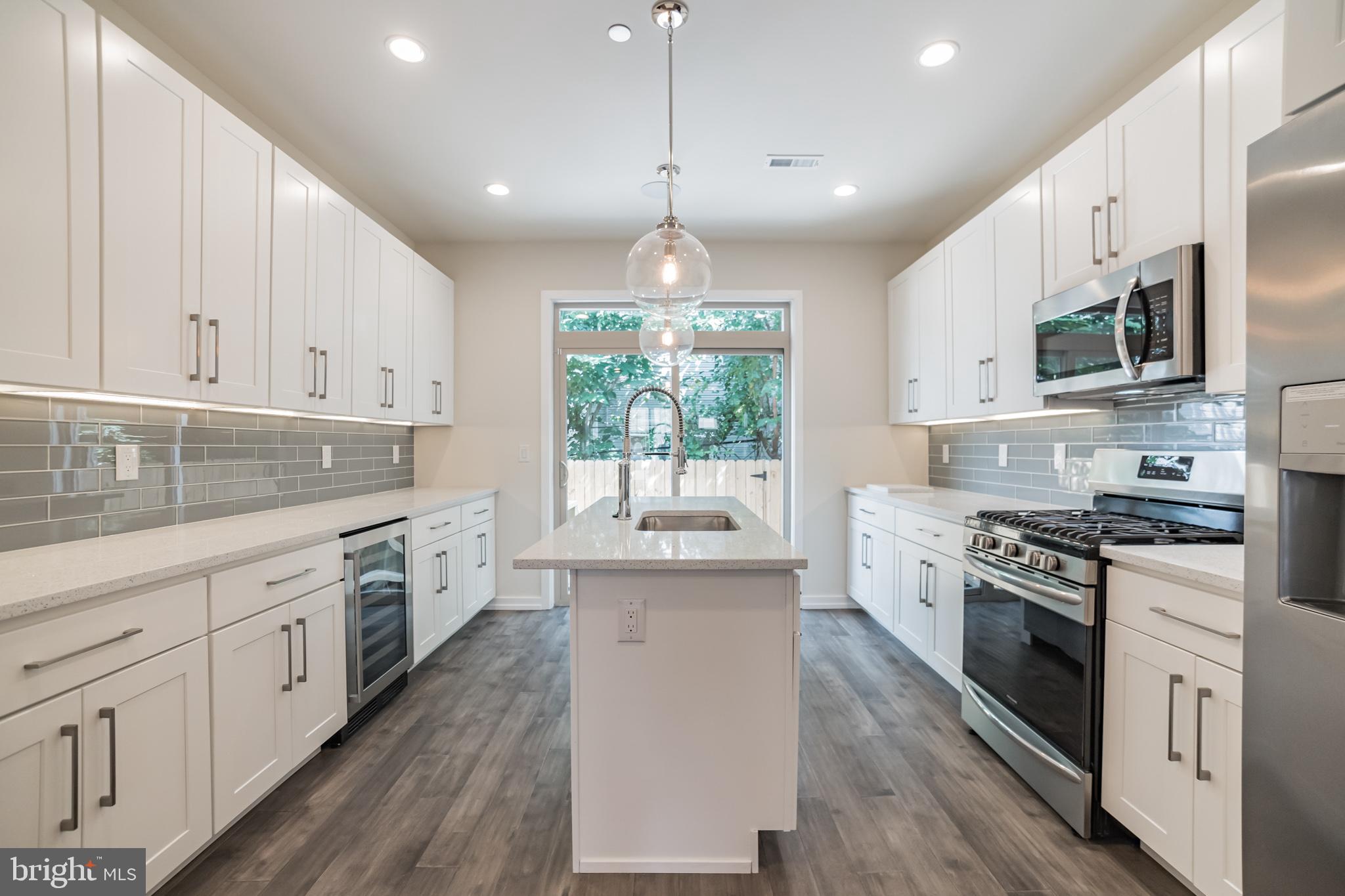 2133 Mifflin Street Philadelphia, PA 19145 - Photo 3 of 6 a kitchen with white cabinets stainless steel appliances a sink and a wooden floor