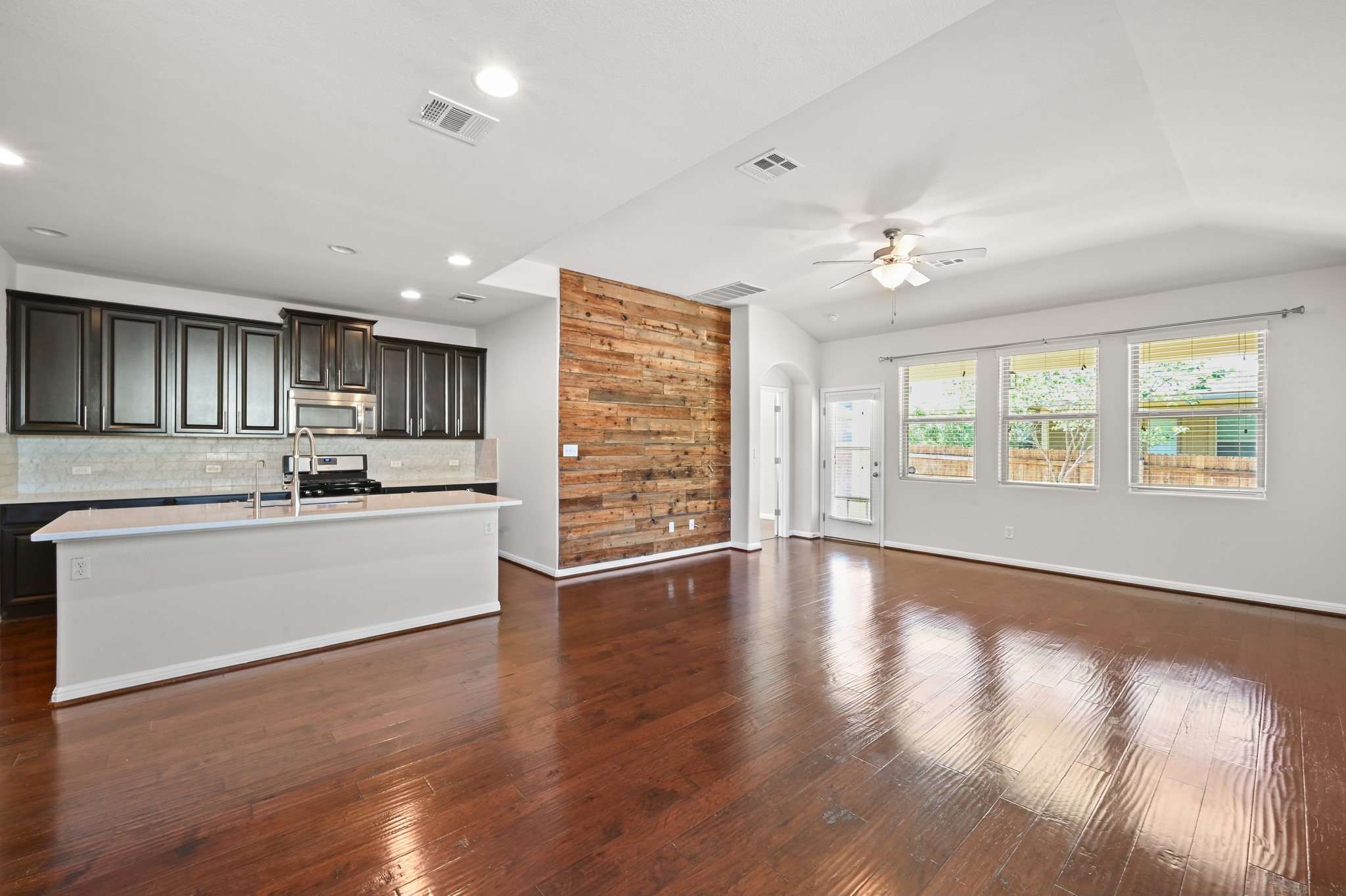 351 Wincliff Drive Buda, TX 78610 - Photo 14 of 40 An open concept living area boasts a rustic wood-paneled accent wall, seamlessly connecting to a modern kitchen.