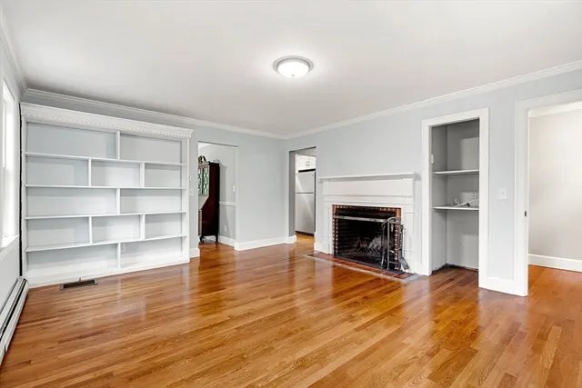 a view of an empty room with wooden floor fire place and windows