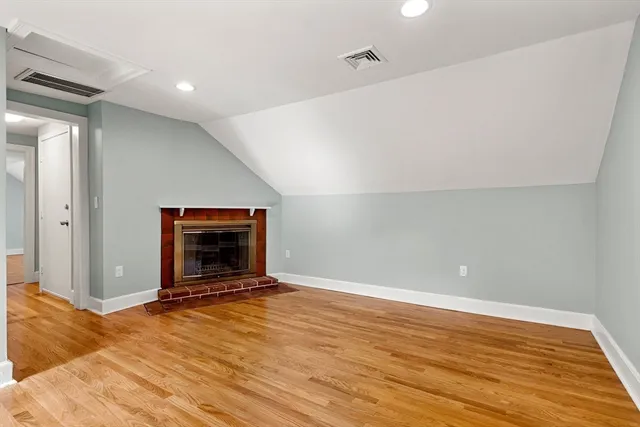 a view of an empty room with wooden floor and a fireplace