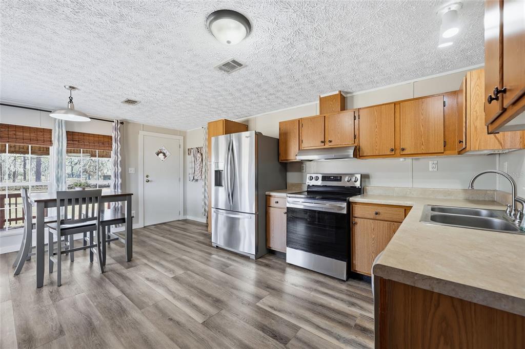 7119 Northeast 24th Loop High Springs, FL 32643 - Photo 5 of 35 a kitchen with stainless steel appliances granite countertop a stove a refrigerator a sink a dining table and chairs with wooden floor